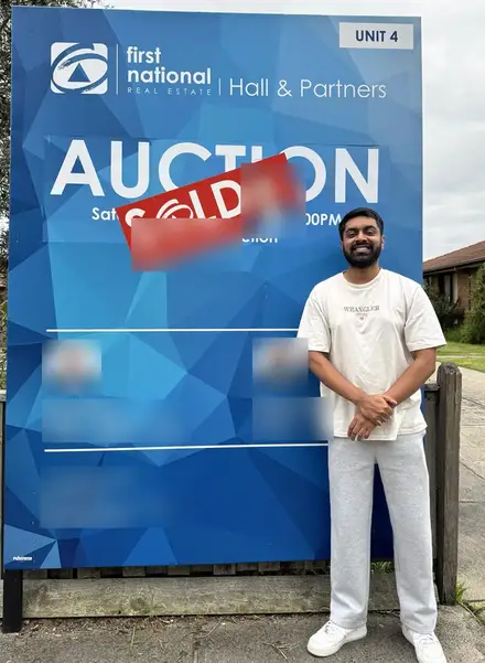 Puri Dewage in front of a SOLD sign